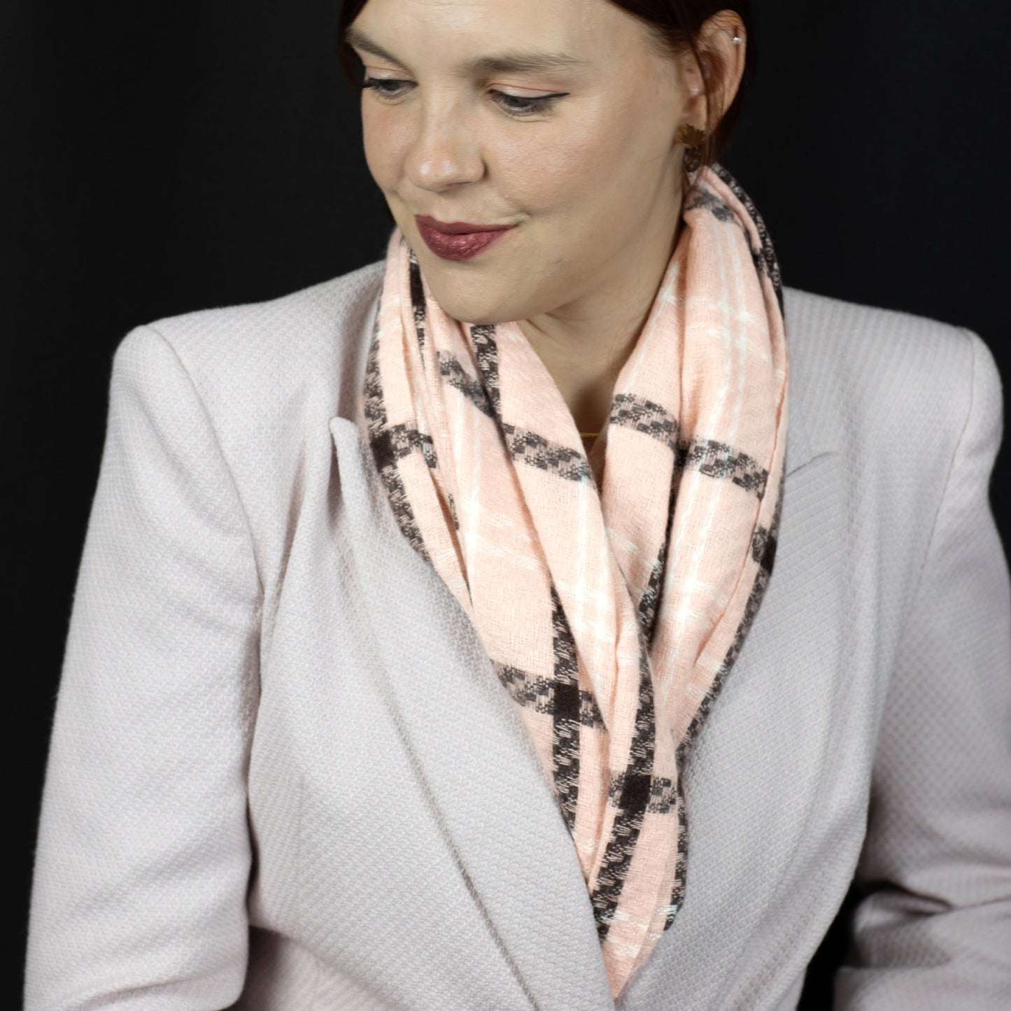 Woman wearing a light gray blazer and a pink scarf with a black pattern against a dark background