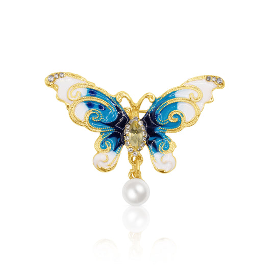 A stunning butterfly brooch featuring blue and white enamel wings adorned with sparkling crystal accents and a single faux pearl drop. Crafted with a gold-plated base, this elegant accessory exudes grace and sophistication, making it the perfect statement piece for both casual and formal wear.