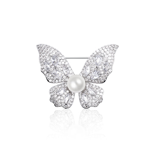 Close-up image of the Celestia Radiance Butterfly Brooch featuring intricately designed wings encrusted with brilliant white crystals and a central pearl bead. The brooch gleams in a rhodium-plated finish, styled in a butterfly shape symbolizing grace and renewal. Perfectly balanced in design and sparkle, it reflects on a white surface to enhance its shimmer, making it a stunning choice for special occasions or elegant everyday styling.