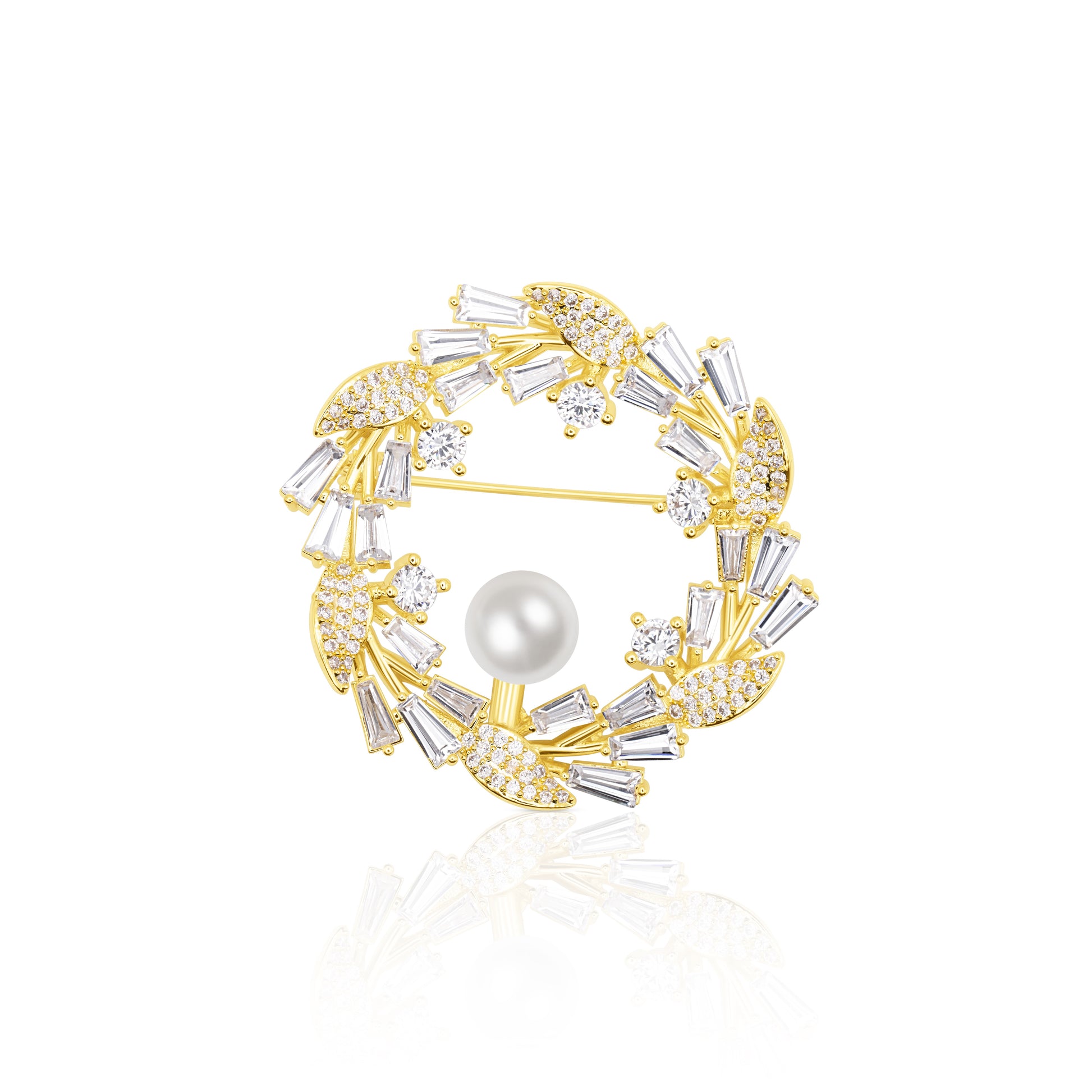 Circular Crystal Wreath Brooch with alternating clear baguette and round stones around a luminous pearl. The gold-plated setting highlights the contrast and symmetry of this festive, winter-ready accessory. Resting on a white reflective surface, it gleams with polished brilliance, making it ideal for holidays, formal events, or refined winter fashion.