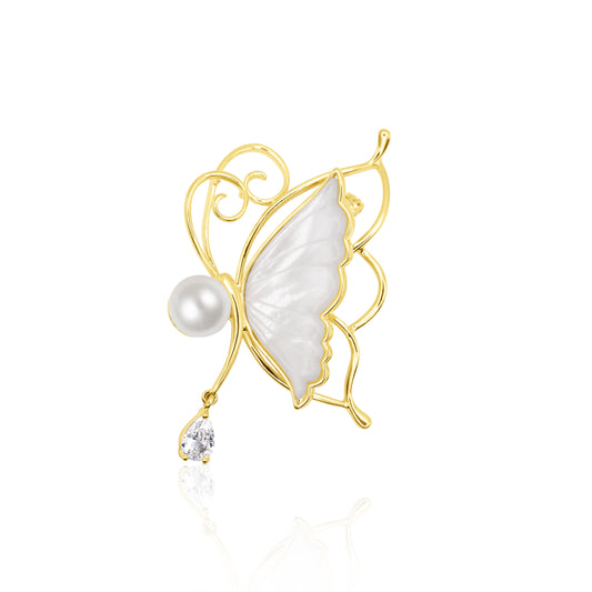 Whisperwing Butterfly Brooch featuring translucent white enamel wings framed in gold, a pearl body at the center, and a single teardrop crystal hanging delicately below. The piece rests on a white reflective background, highlighting its fairy-like elegance and subtle sparkle. A light and enchanting accessory perfect for weddings, spring events, or soft glam fashion.